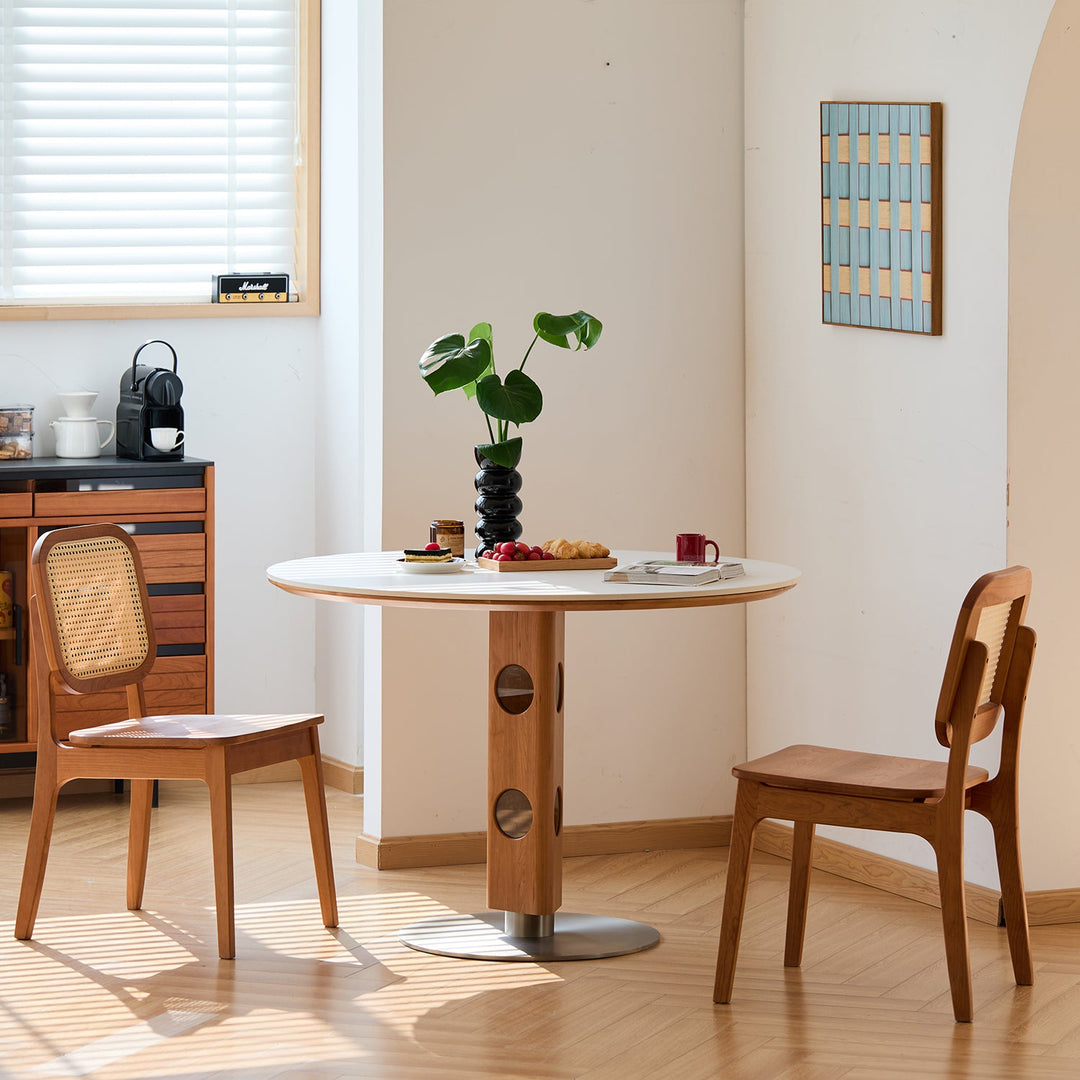 Round wood dining table with circular cut-out pedestal base, styled with rattan chairs and warm lighting, ready in stock for immediate setup.